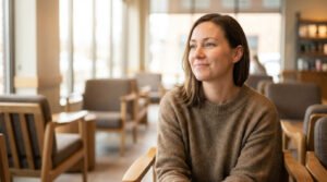 Woman with serene smile in a modern, warm-lit cafe, conveying thoughtful confidence and quiet contentment.