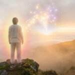 Person with glowing aura on mountain peak at dawn, overlooking clouds. Golden & purple light converges in sky, symbolizing positive attraction.