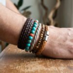Poignet d'homme avec une superposition de bracelets : cuir marron tressé, perles turquoise, bracelet en métal et perles de bois.