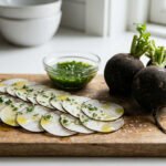 Radis noirs entiers et tranchés, assaisonnés d'huile, herbes et sel, avec une sauce verte sur une planche en bois. Fond de cuisine lumineux.