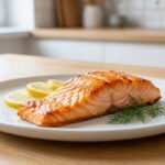 Un filet de saumon doré au four, garni de citron et d'aneth sur une assiette blanche, posé sur une table en bois.