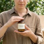 Une personne tenant un flacon de compléments alimentaires étiqueté « BERBERINE CAPSULES » devant un arrière-plan naturel.
